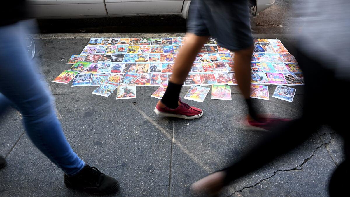 Pedestrians walk past DVD covers along Maple Avenue in the Fashion District in Los Angeles.