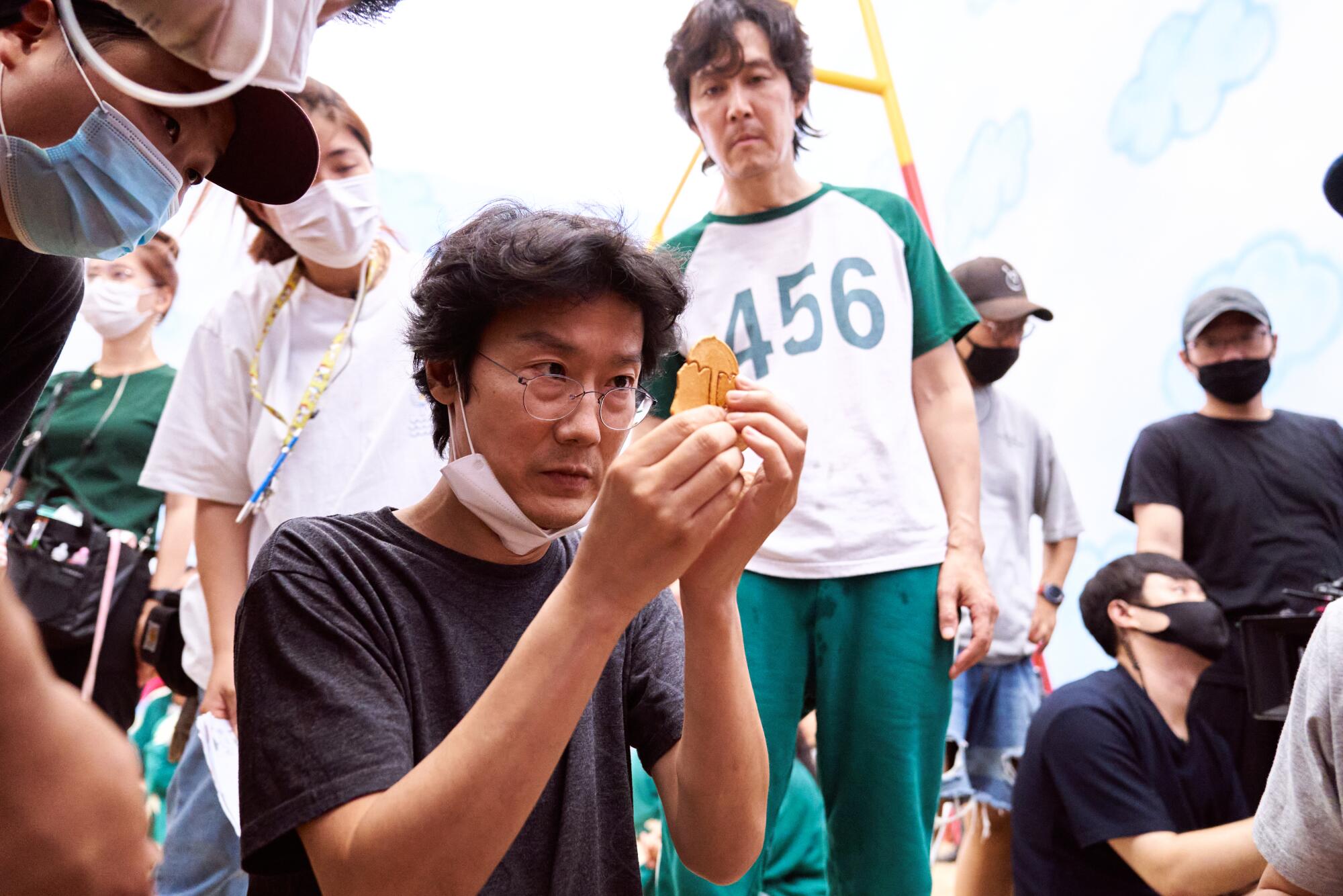 A man examines a small prop on set while cast and crew look on.