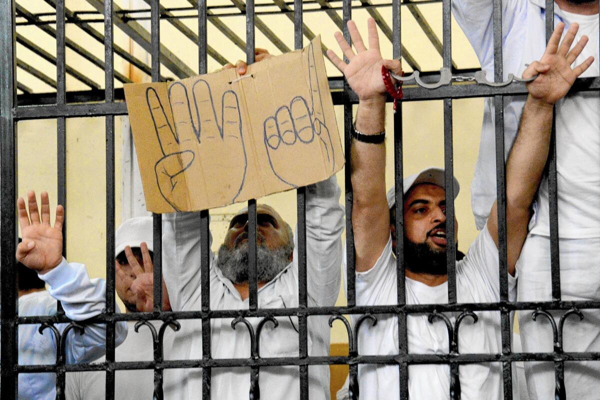 Islamist defendants react as harsh sentences are handed down at a mass trial in Alexandria, Egypt. The gesture indicated on the sign has become a symbol for Cairo's Rabaa al Adawiya mosque, where Islamist demonstrators faced off with government forces in August.