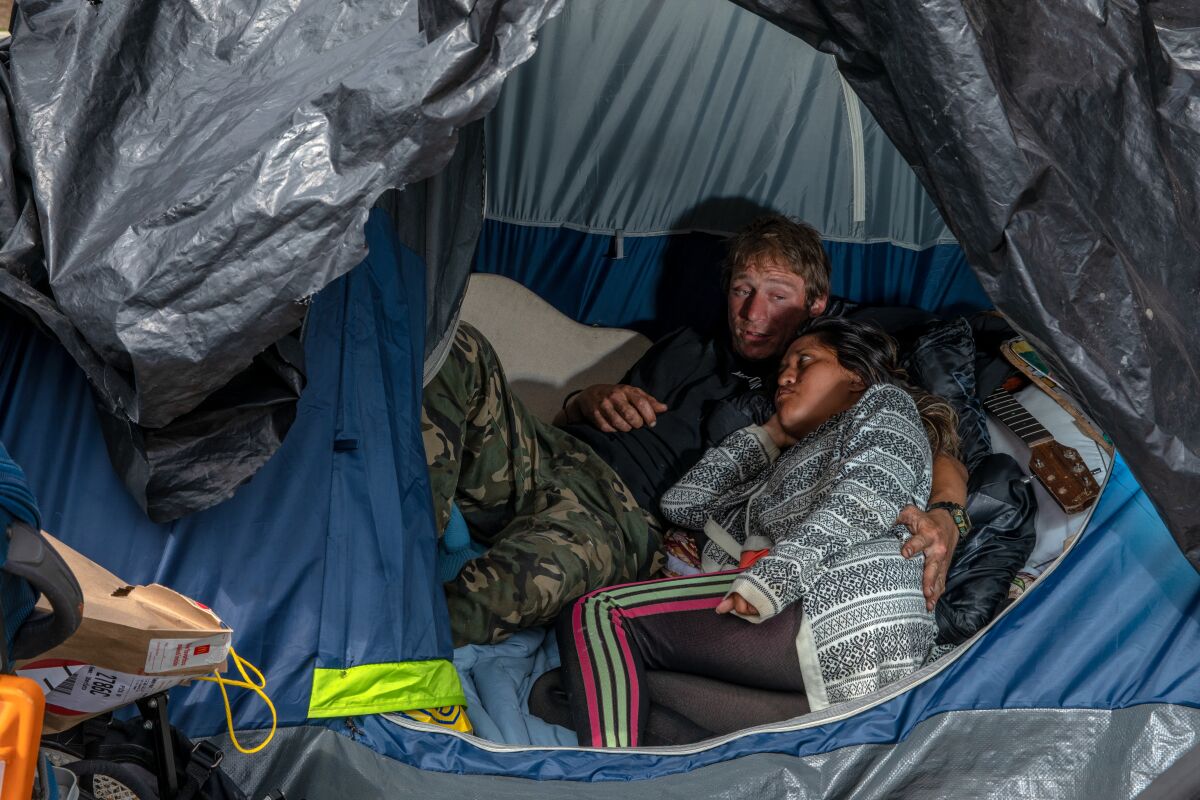 A man puts his arm around a woman as they lie in a tent