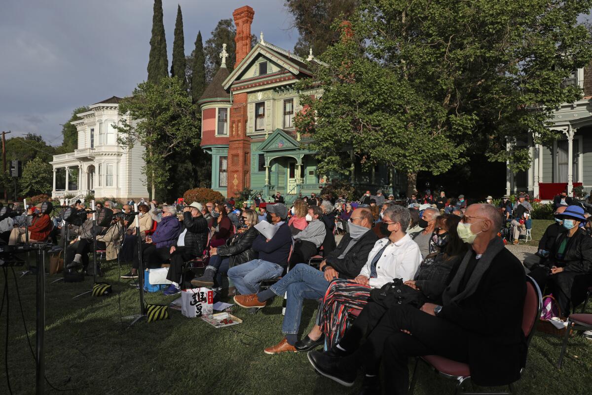 Many people seated in chairs on the front lawn of a house 