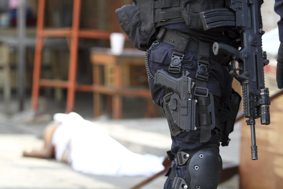 A police officer armed with multiple weapons stands in front of a body covered with a sheet