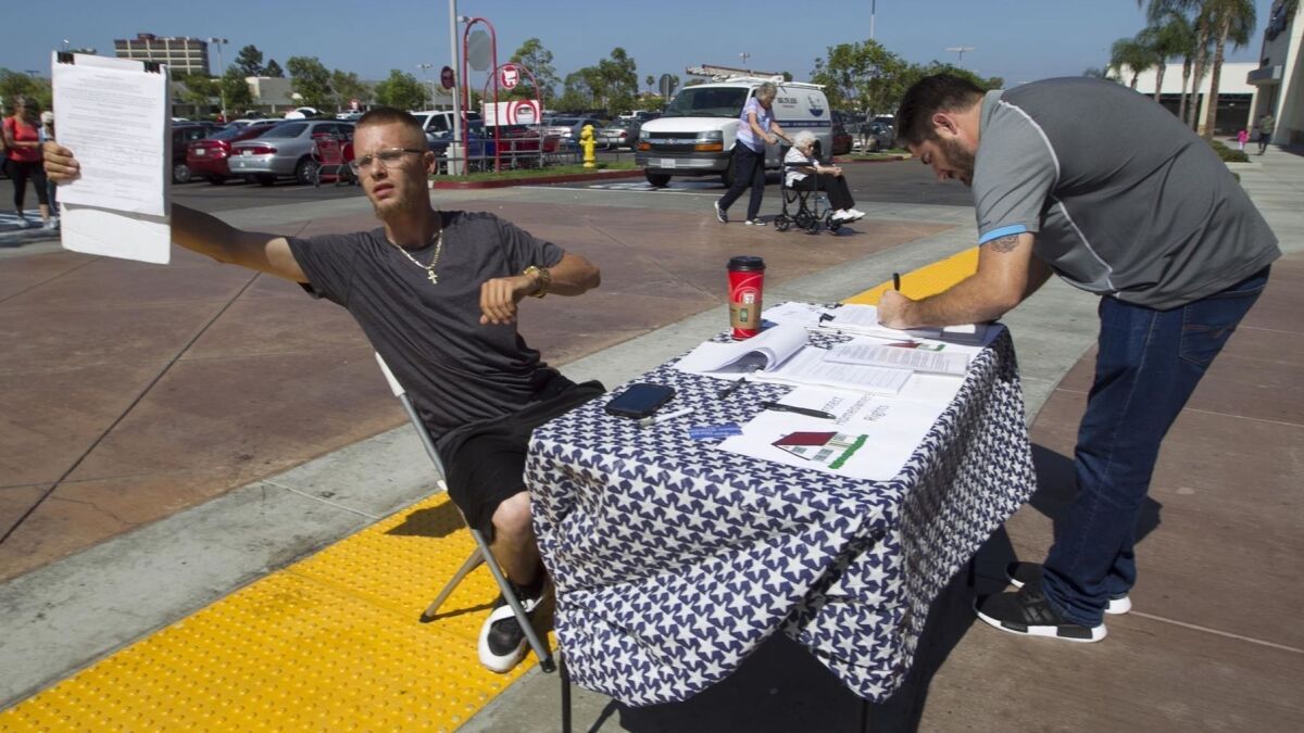 Signature gatherer William Collins calls out to people exiting the Target store on Balboa Avenue while Jon McKinney from Chollas View signs a petition to force a public vote that would decide the fate of vacation rentals in San Diego.