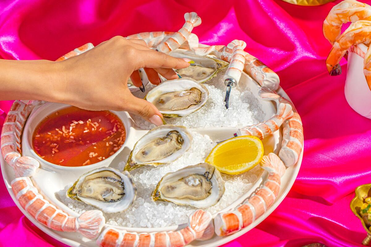 A photo of a hand reaching for raw oysters on a shrimp-themed platter.