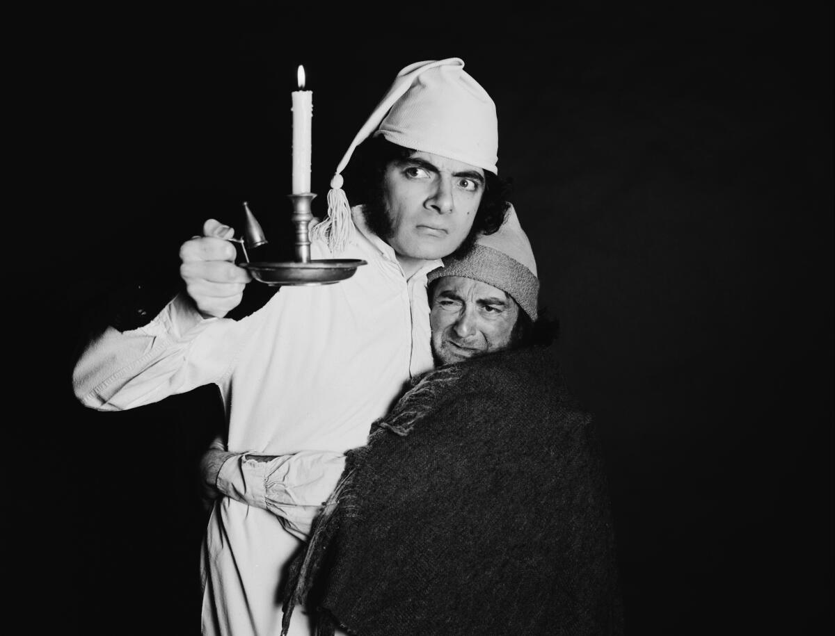 Two men in night clothes clutch each other. One holds up a lighted candle.