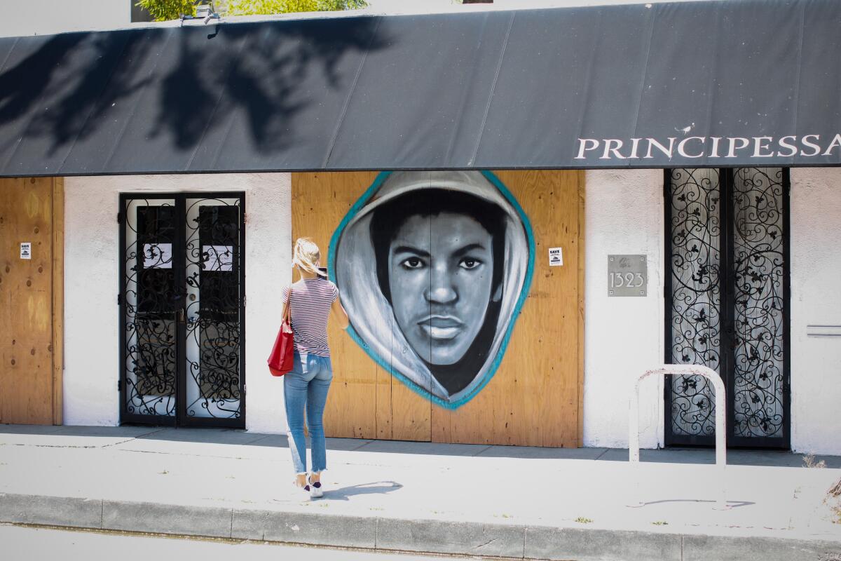 A woman stops to photograph a mural of Trayvon Martin painted on plywood of a building
