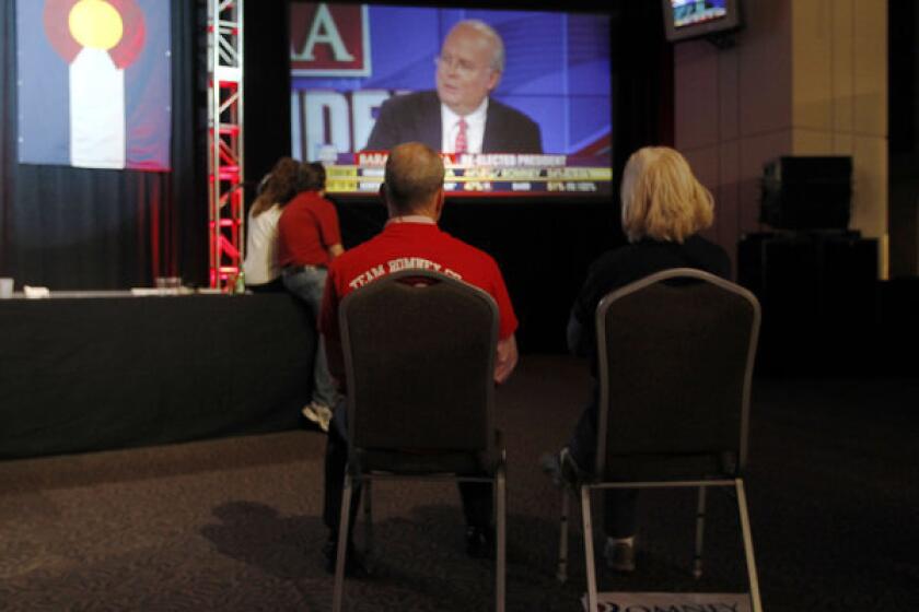 A couple sits on chairs in a near-empty room to watch Fox News commentator Karl Rove on a big-screen television during a Republican Party election night gathering in the club level of Sports Authority Field at Mile High in Denver on Tuesday.