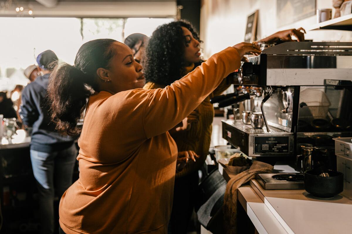 Two women work behind the counter of a coffee shop.