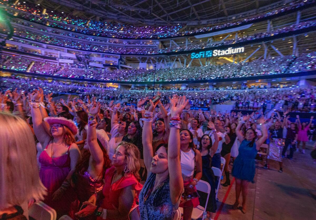 Fans raise their arms amid the colored lights during a concert at a stadium.