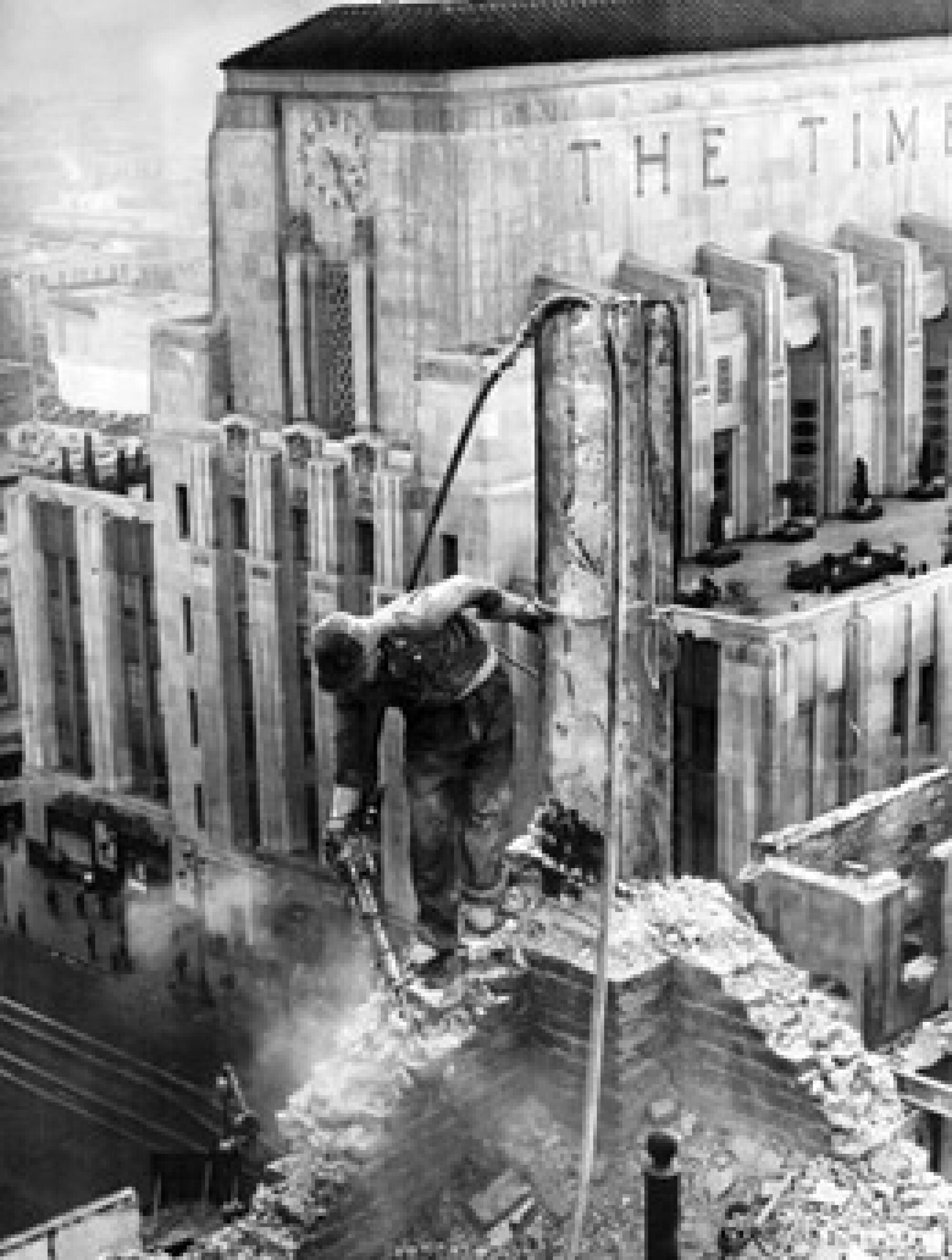 A black-and-white photo of a worker jackhammering on top of a building's remains, a stately Art Deco building behind him.