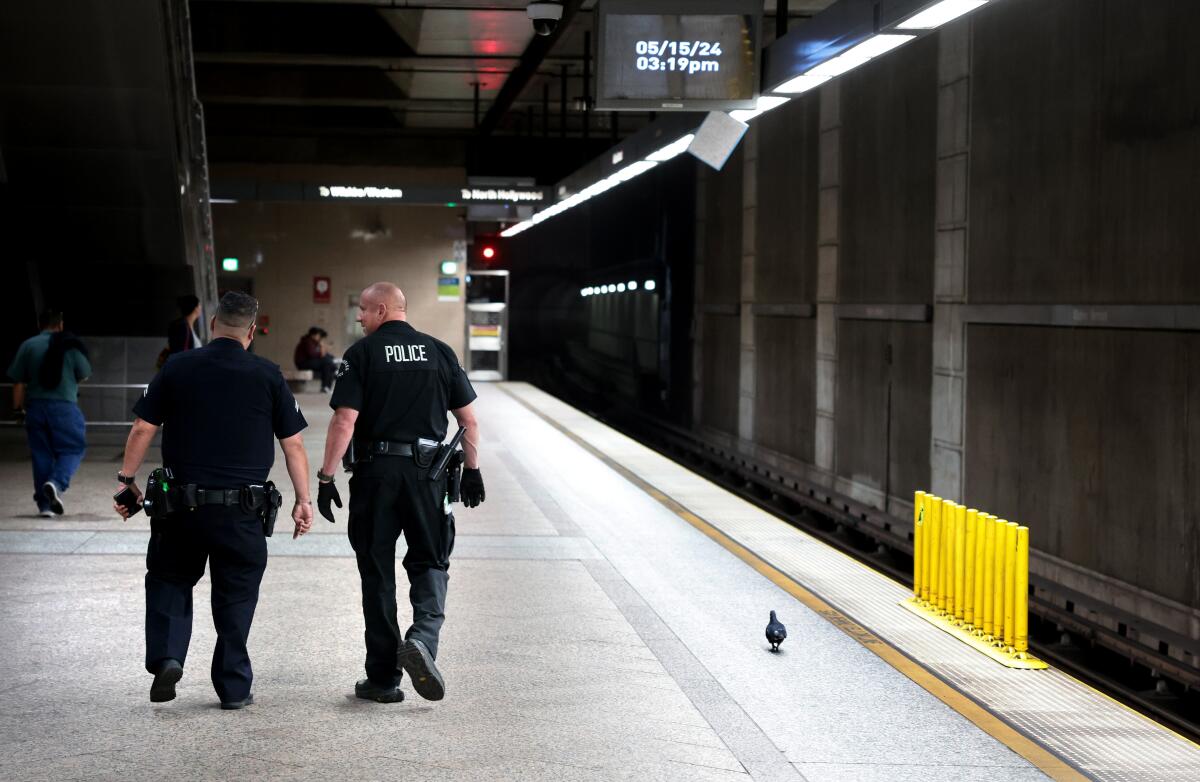 Two men in police uniforms walk on a subway platform.
