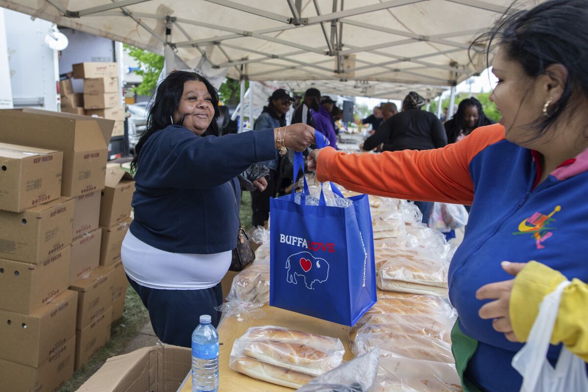 Yvonne King, left, hands out bags of breads to community members near the Tops Friendly Market, Tuesday, May 17, 2022, in Buffalo, N.Y. While Tops is temporarily closed during the shooting investigation, the community is working to make sure residents don’t go without. (AP Photo/Joshua Bessex)