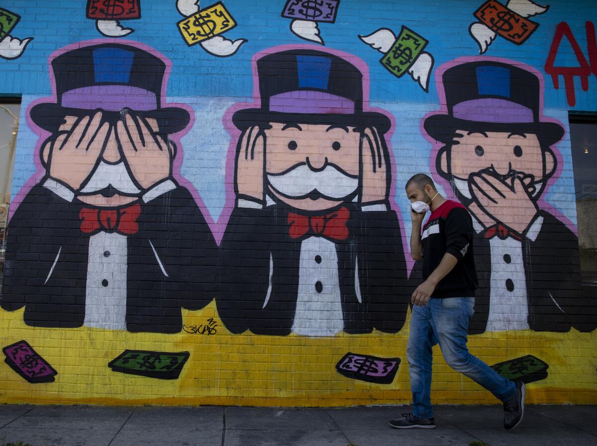 A person wearing a protective mask walks by a mural on Melrose Avenue in Los Angeles.