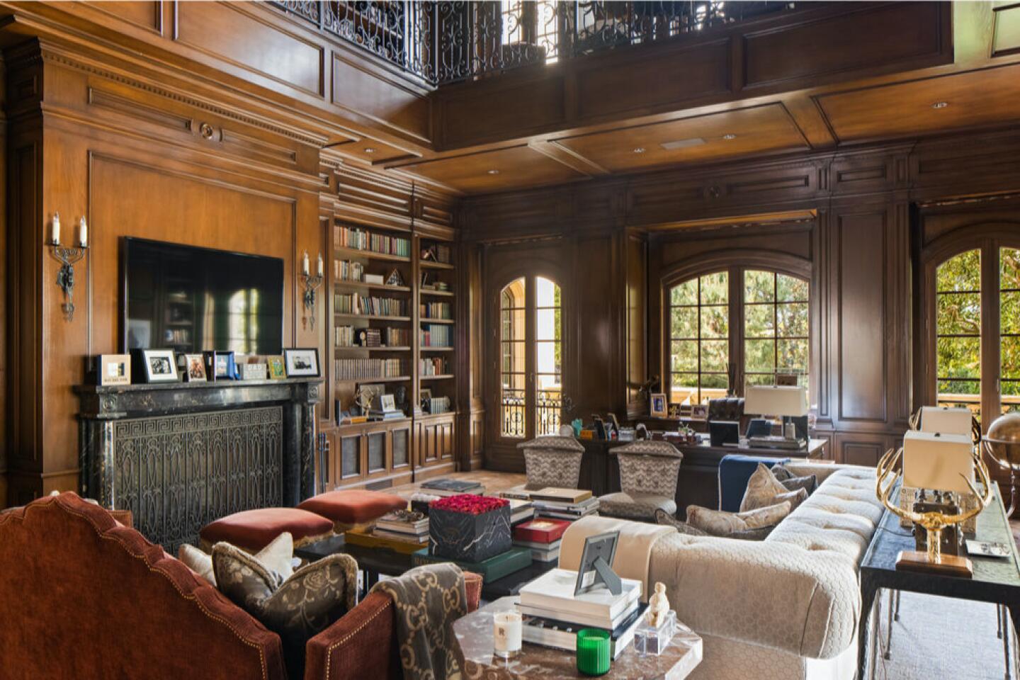 The wood-paneled library with shelves of books and seating with windows overlooking greenery.