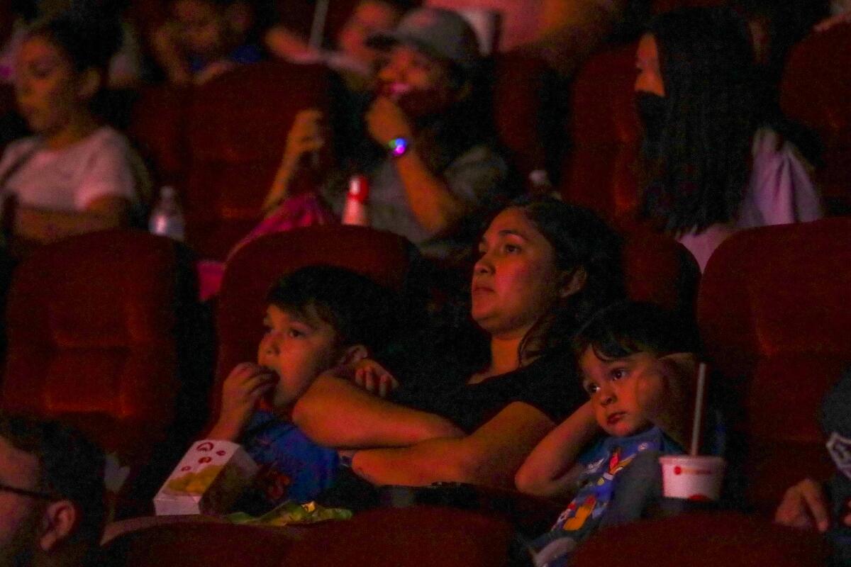 A woman and two kids watch a movie in a theater.