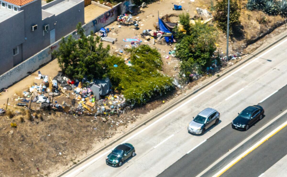 A group of tents spread next to a freeway as cars pass by.
