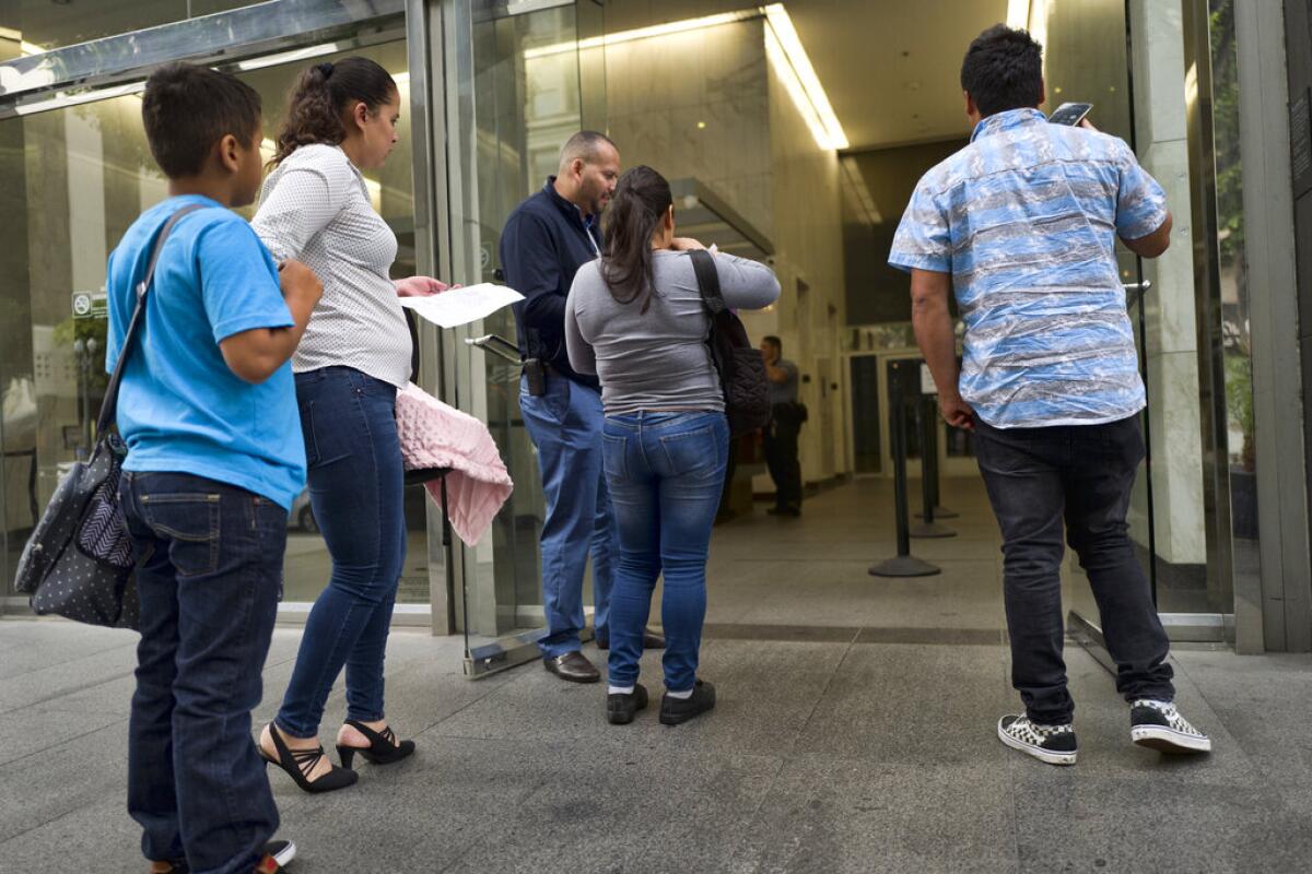 ARCHIVO - En esta fotografía del 30 de mayo de 2019, unos migrantes muestran sus documentos para entrar a un tribunal de inmigración en un edificio de Los Ángeles.