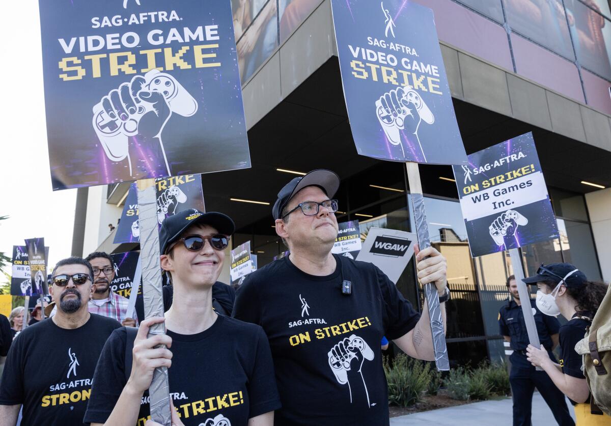 A group of people marching and carrying picket signs that read, "SAG-AFTRA video game strike"