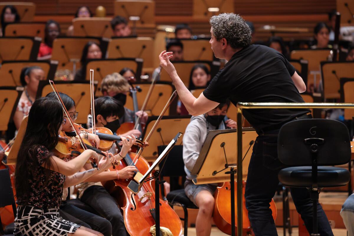 Gustavo Dudamel, standing on a podium, gestures towards teenagers playing violins and cellos