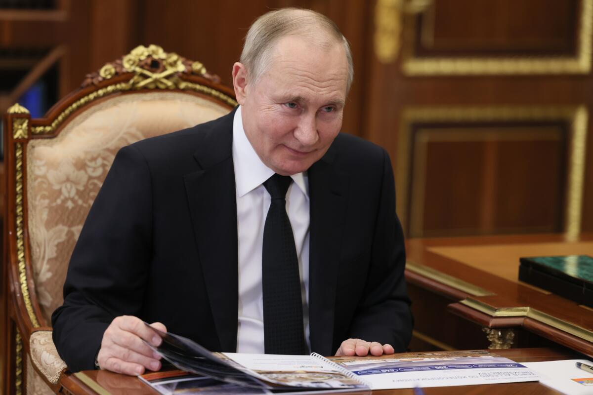 Russian President Vladimir Putin smiles while sitting at a desk