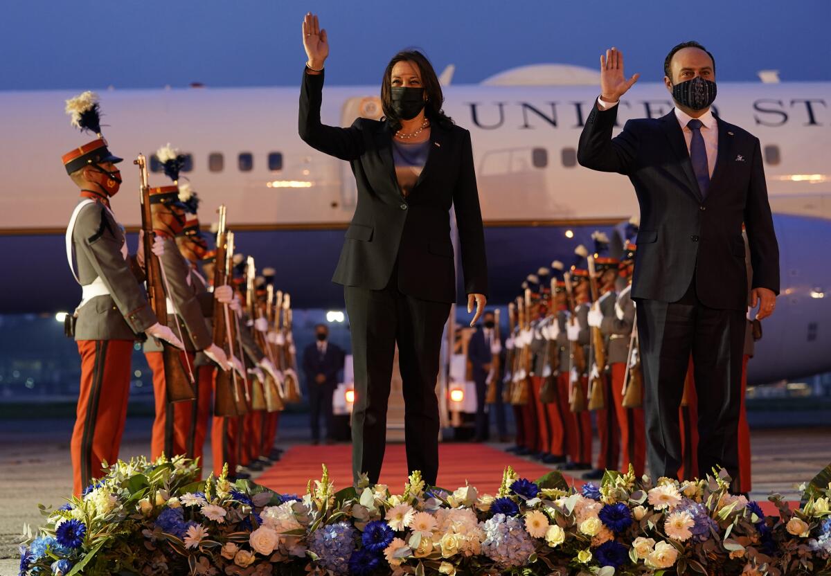 Kamala Harris and Guatemala's Pedro Brolo wave on a runway with a red carpet, uniformed troops and Air Force Two behind them