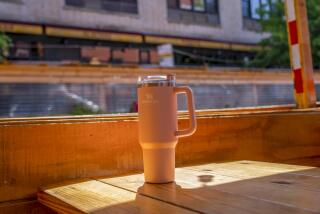 A Stanley tumbler is set on a restaurant table in the sunshine.