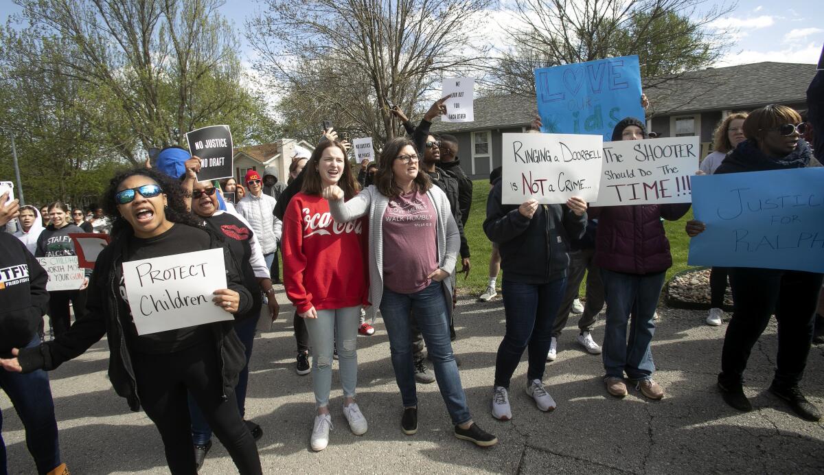 People march on a residential street, some carrying signs that say "Protect Children" and "Ringing a Doorbell is Not a Crime"
