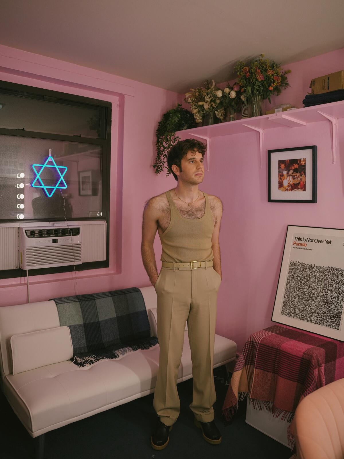 A man stands in a pink room, with a blue neon Star of David in the window.