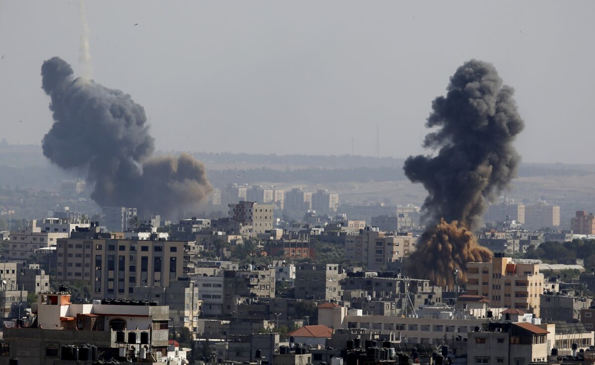 Two plumes of gray smoke billow behind multistory buildings.
