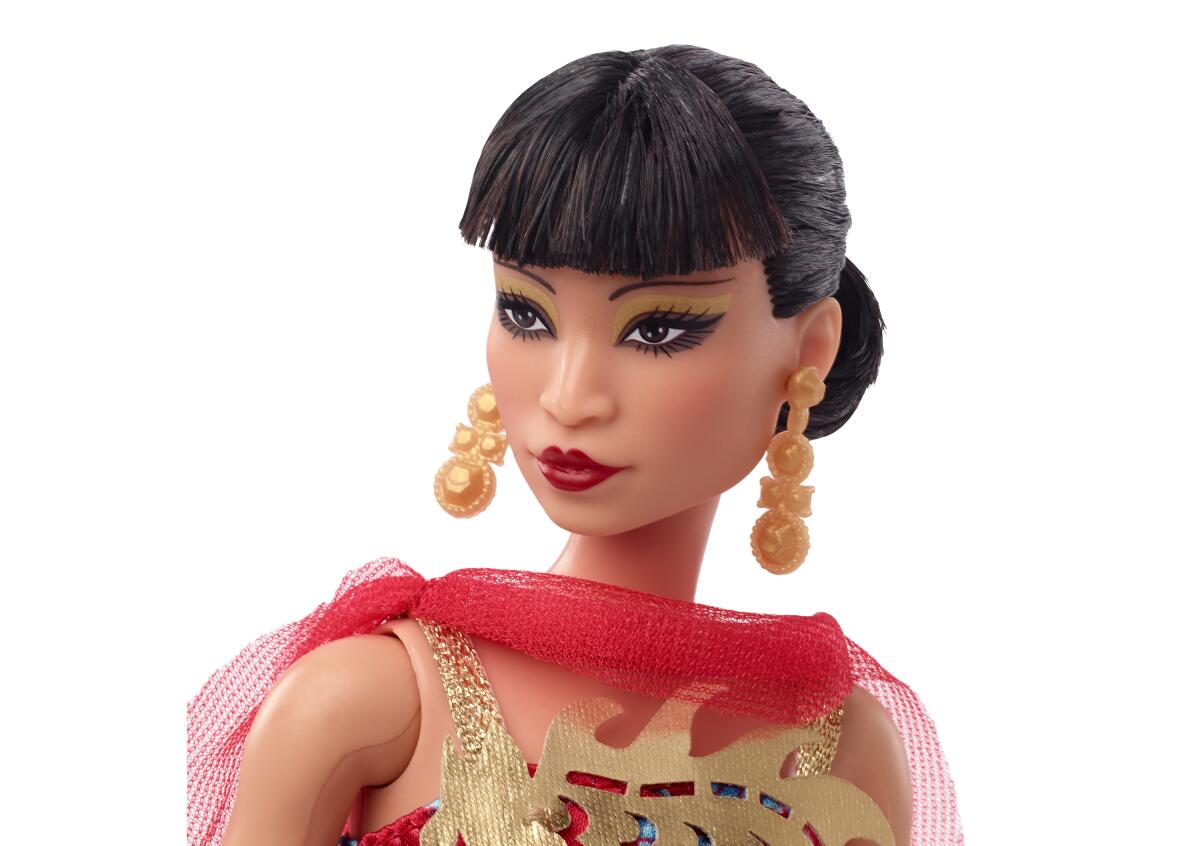 A Barbie doll resembling Anna May Wong, accessorized with gold dangly earrings and a red scarf
