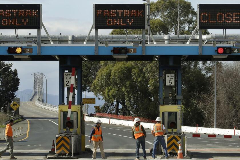 Caltrans workers walk in front of a toll plaza at the closed Richmond-San Rafael bridge Thursday, Feb. 7, 2019, in Richmond, Calif. the bridge connecting the San Francisco Bay Area has been closed after large chunks of concrete fell from the upper deck to the lower deck. (AP Photo/Ben Margot)
