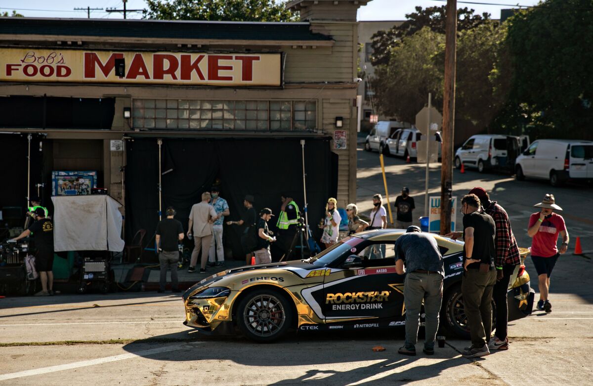 People around a sports car with the Rockstar Energy Drink logo parked in the street outside a corner store