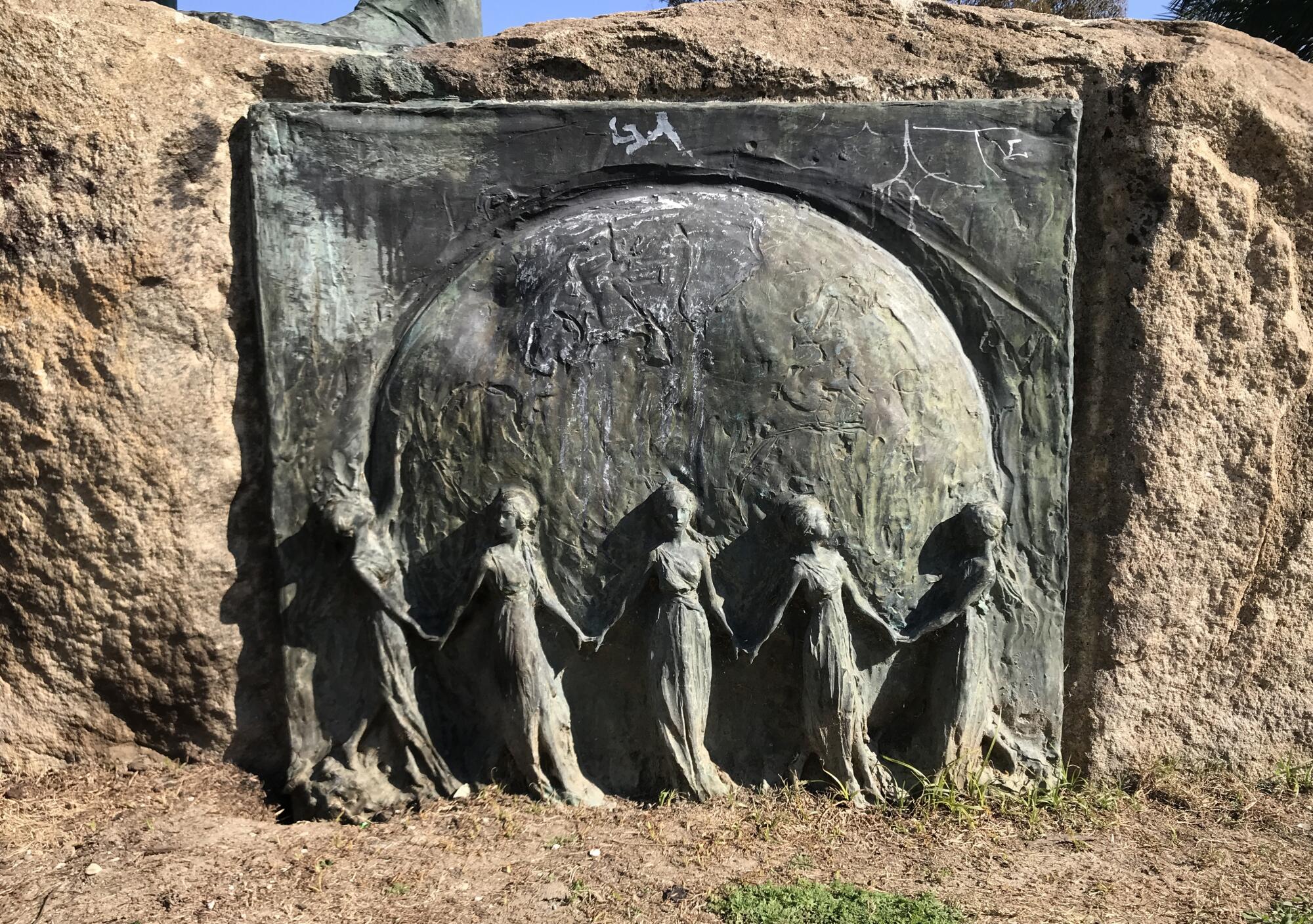 A small frieze of five gowned women holding hands before the outline of the world that honors 
