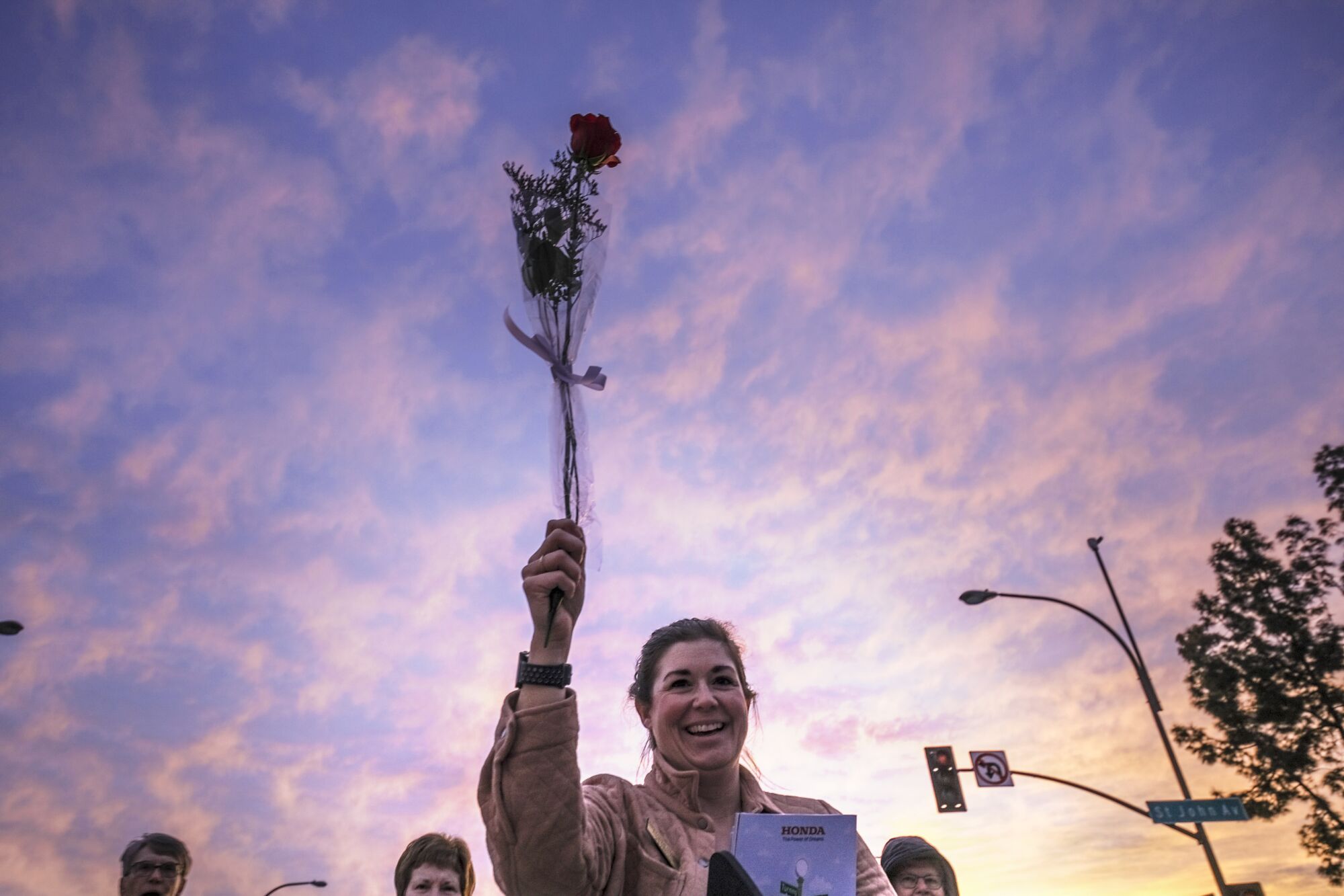 A woman holds a rose against a pink sunrise.