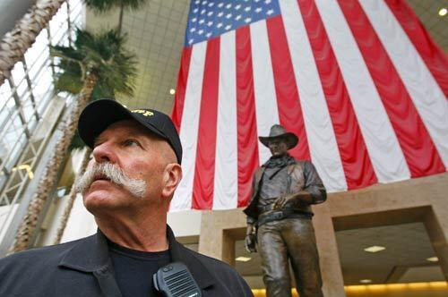 Orange County sheriff's volunteer John Reichardt, 68, a retired postal worker from Santa Ana, pauses in front of a statue of John Wayne while on patrol to help people find their way around John Wayne Airport. Reichardt, who volunteers about 30 hours a week, says he was hurt when Sheriff Sandra Hutchens decided to recall the badges issued to volunteers. It felt like a punch to the stomach, he says.