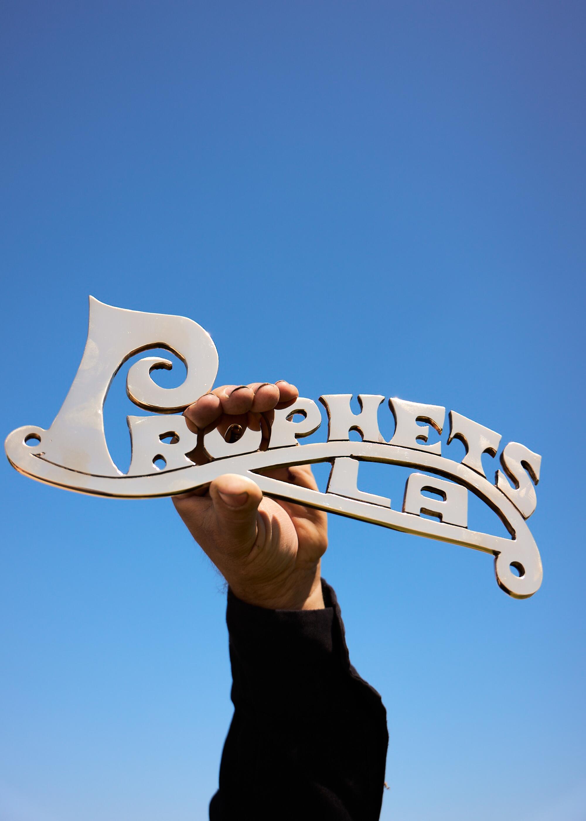 ”Prophets LA” lowrider plaque designed by Pinche Kid held up to the sky by plaque maker David Lopez