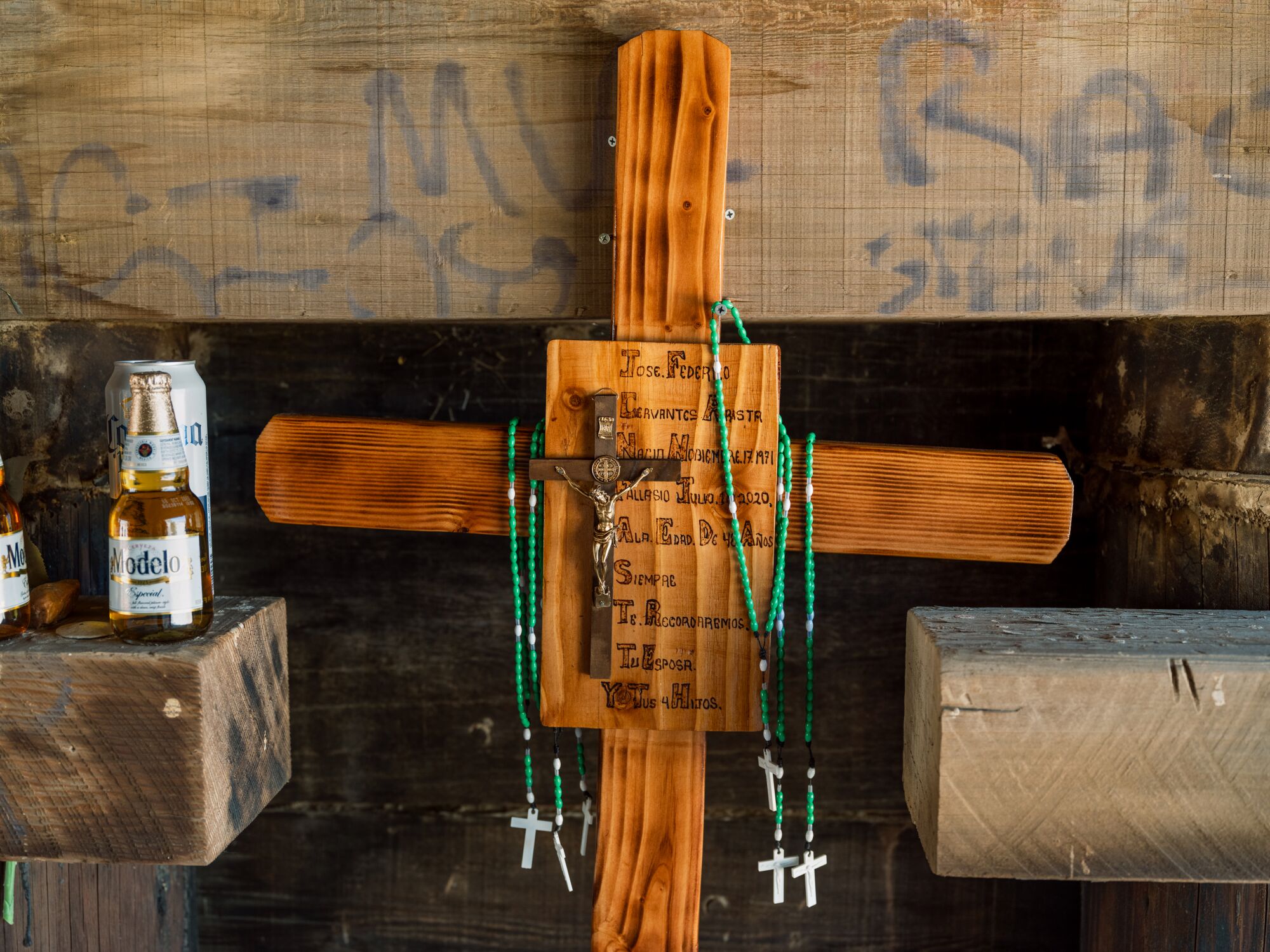 A horizontal frame of a wooden cross with another crucifix attached to its center and several rosary beads hanging on sides