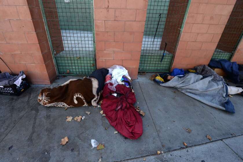 Homeless people sleep on the street on skid row.