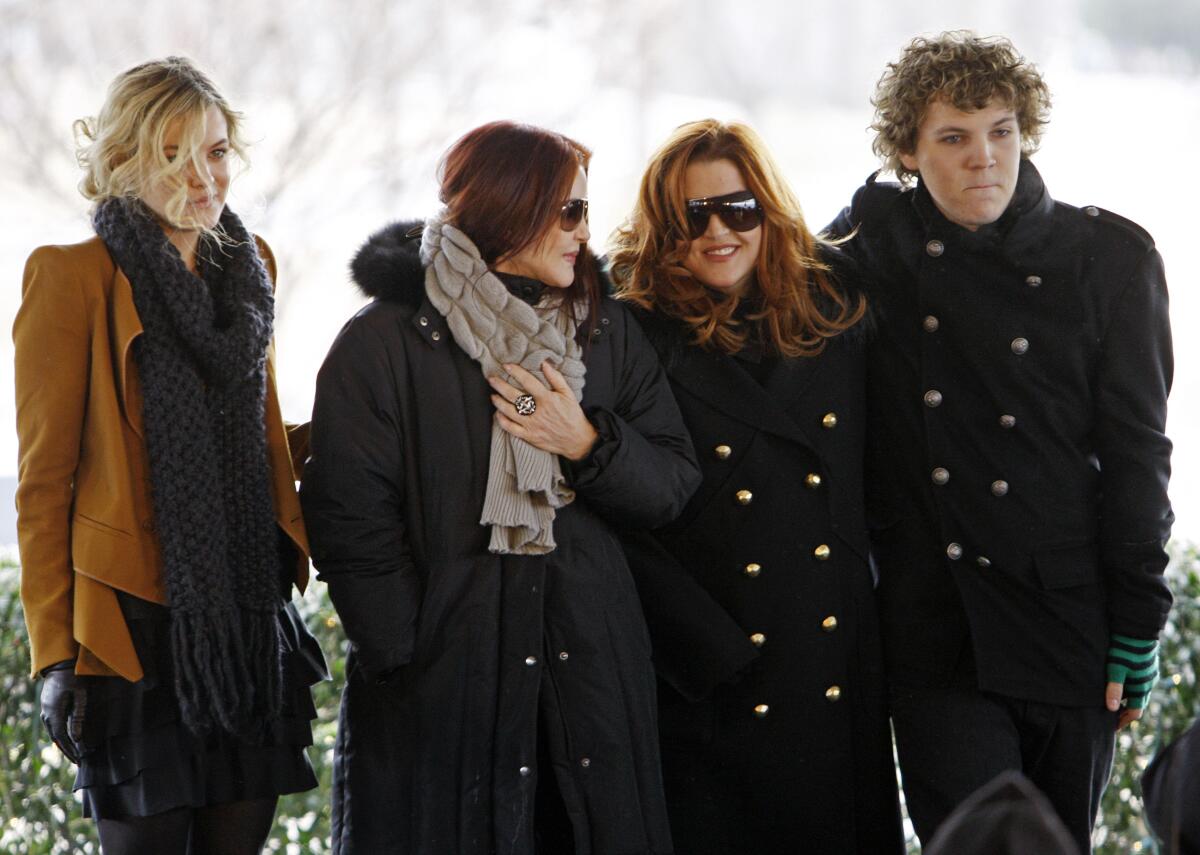 Three women bundled up in coats and a man with curly hair in a dark coat.