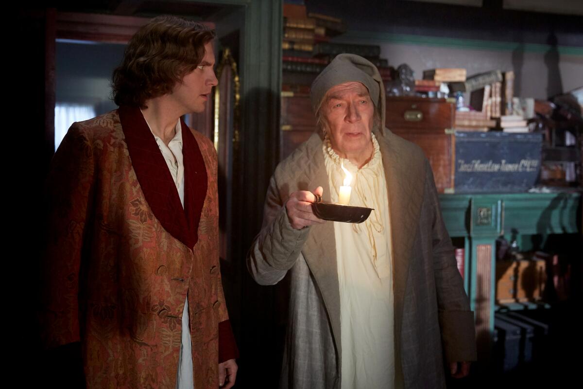 Two men stand together in night clothes and robes, one in a sleeping cap and carrying a lighted candle.