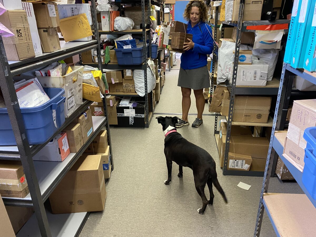 A woman holds boxes inside a parcel depot as a dog looks on.