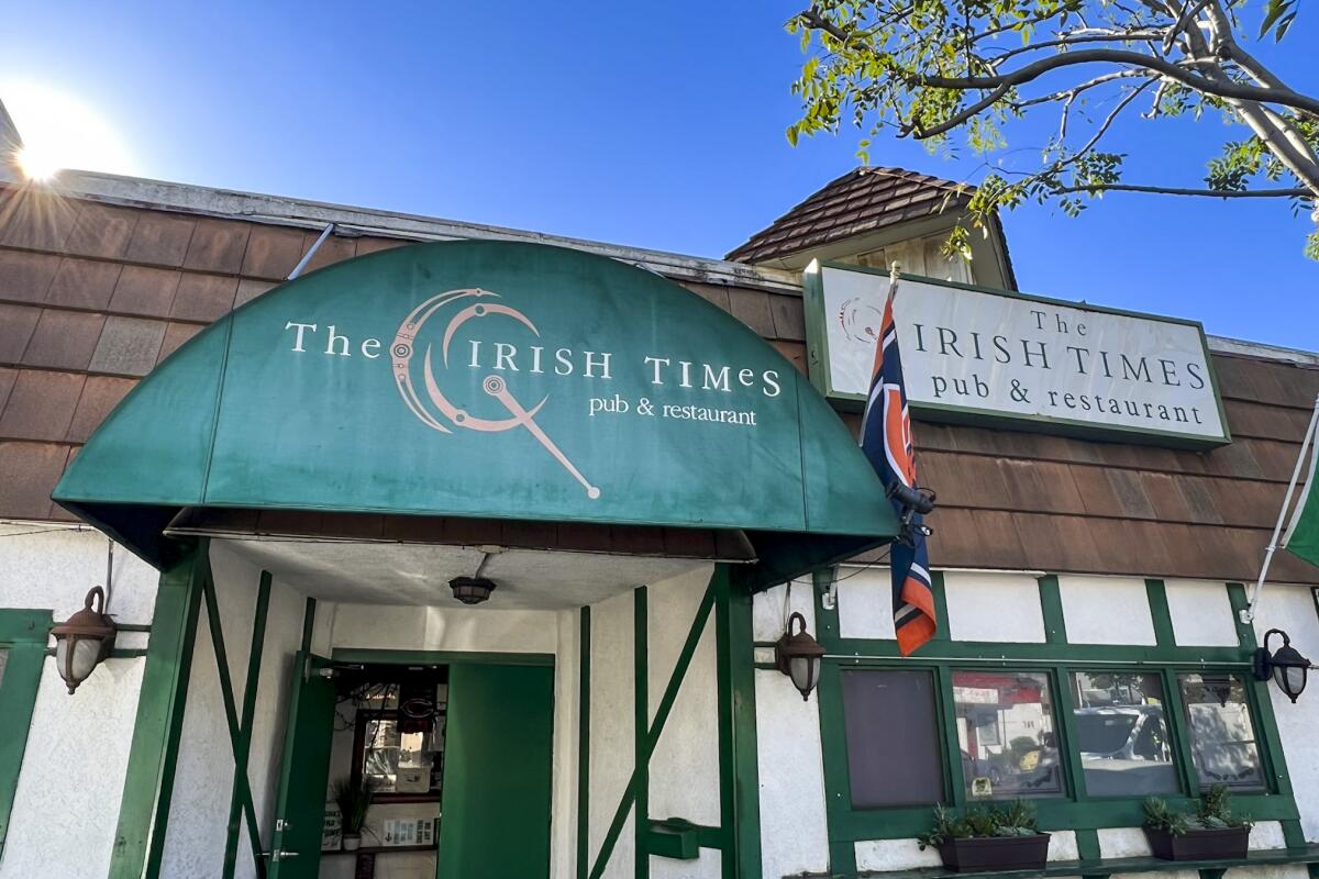 A bar exterior in daylight with a green awning that reads the Irish Times Pub & Restaurant.