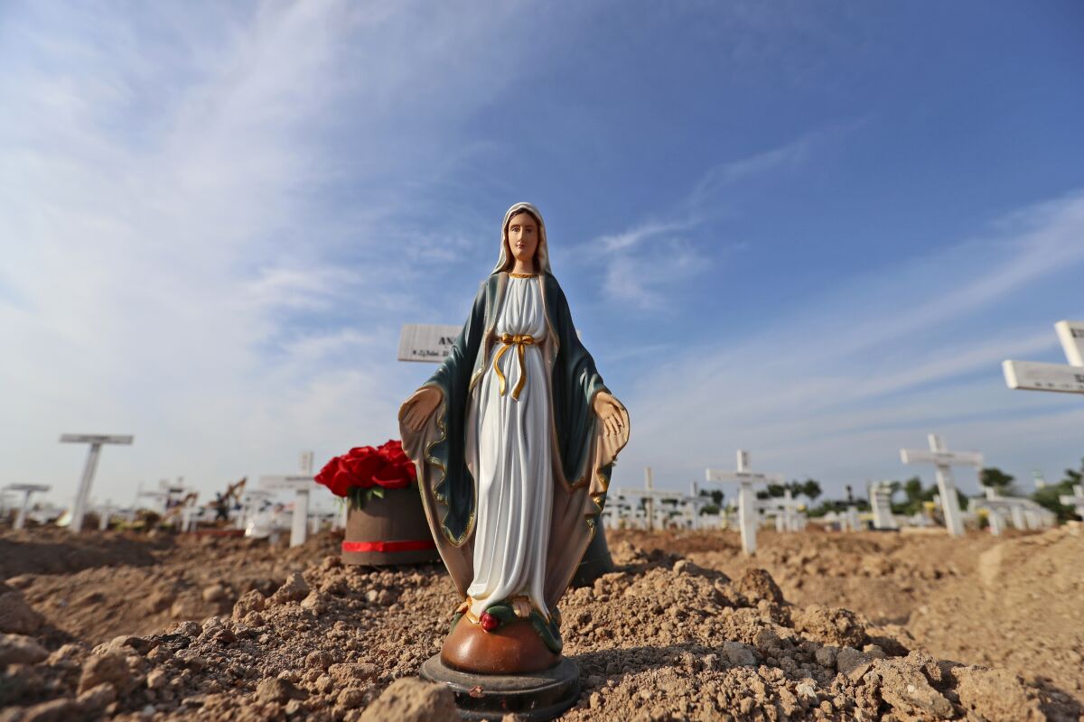 A statue of Virgin Mary is placed on the grave of a woman who died of COVID-19 at Rorotan Cemetery in Jakarta, Indonesia, Wednesday, Sept. 1, 2021. In the graveyard on Jakarta's outskirts, portraits of the dead, bouquets of flowers and other mementos serve as reminders of the deadly coronavirus wave that battered Indonesia over the summer. (AP Photo/Achmad Ibrahim)