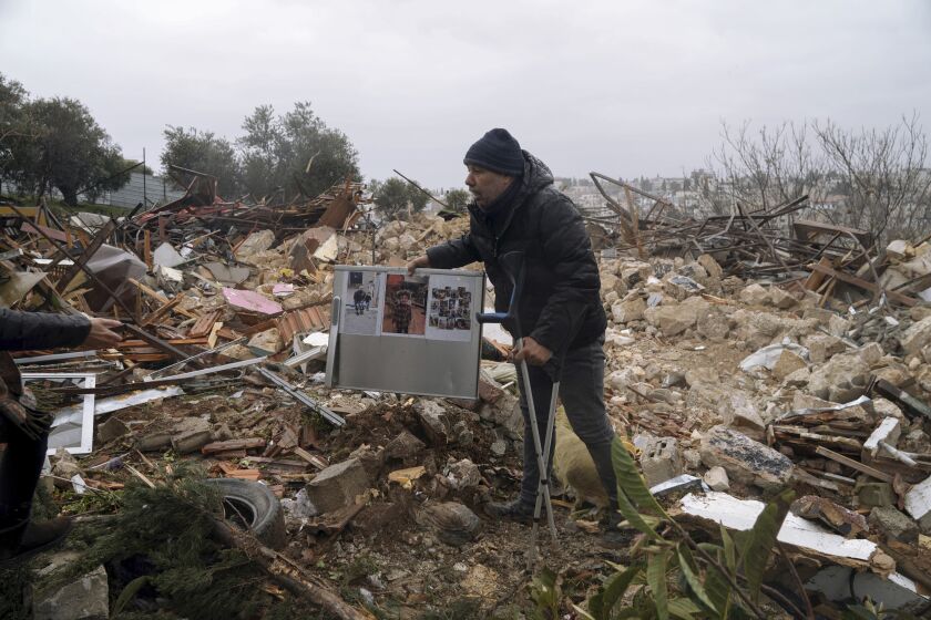A Palestinian man carries family photos at the ruins of a house demolished by the Jerusalem municipality, in the flashpoint east Jerusalem neighborhood of Sheikh Jarrah, Wednesday, Jan. 19, 2022. Israeli police on Wednesday evicted Palestinian residents from the disputed property and demolished the building, days after a tense standoff. (AP Photo/Mahmoud Illean)