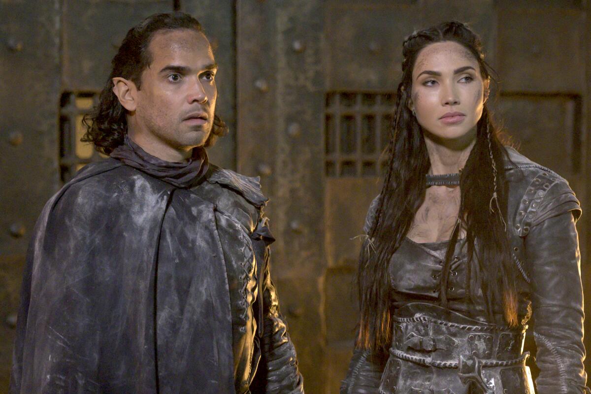 A man and a woman in brown futuristic leather outfits in "The Outpost" on The CW.
