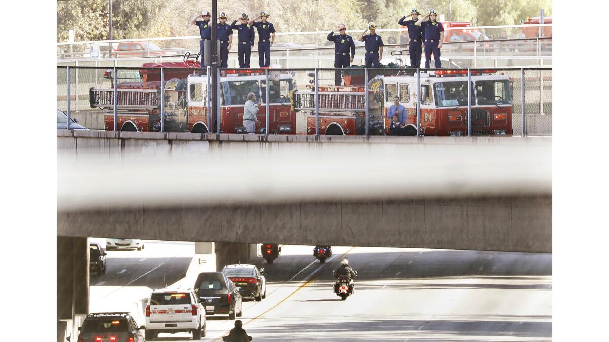 Burbank firefighters salute as the funeral procession travels through Burbank on its way to San Diego.