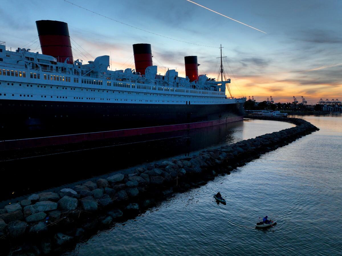Amid cool weather, people fish from a kayaks with a view of the historic RMS Queen Mary ocean liner.