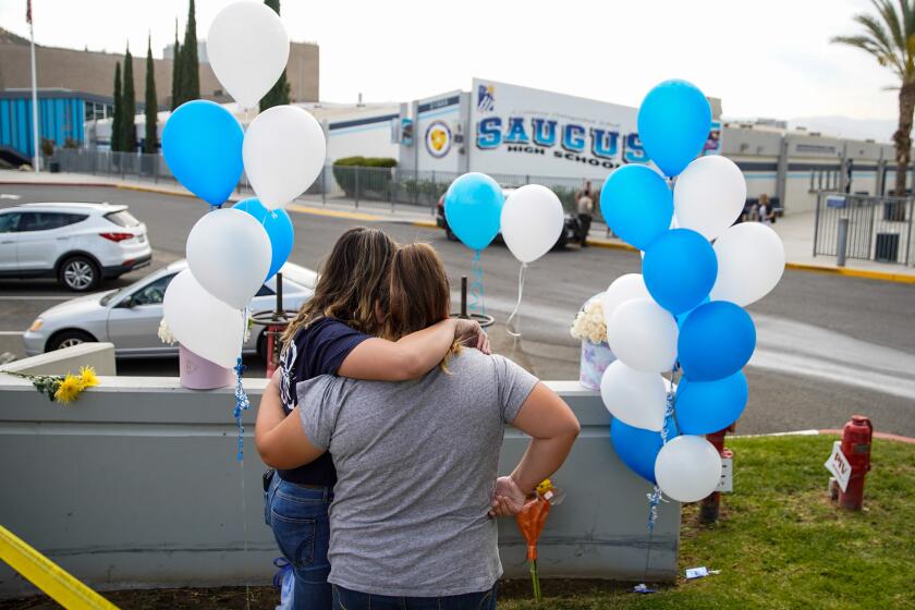 SANTA CLARITA, CALIF. - NOVEMBER 15: Hailey Stuart, a freshman at Saugus High School, and her sister, Ashley Stuart hug after placing flowers and paying their respects at a memorial at Saugus High School on Friday, Nov. 15, 2019 in Santa Clarita, Calif. The school remains closed a day after a shooting where a teenage boy gunned down fellow students on November 14, 2019. (Kent Nishimura / Los Angeles Times)