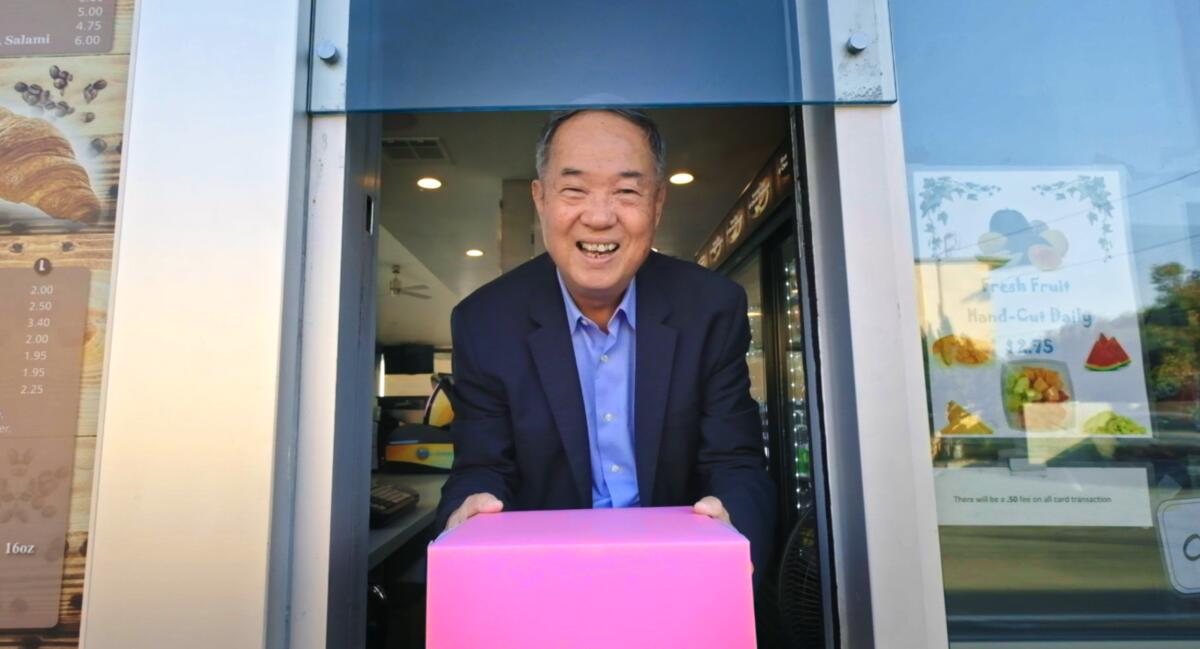 "Donut King" Ted Ngoy passes a pink box through a drive-up window