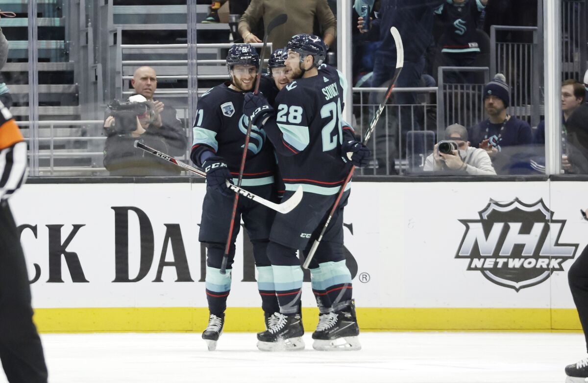 Seattle Kraken center Alex Wennberg, left and defenseman Carson Soucy (28) embrace left wing Jared McCann after he scored against the Dallas Stars during the first period of an NHL hockey game Sunday, April 3, 2022, in Seattle. (AP Photo/John Froschauer)